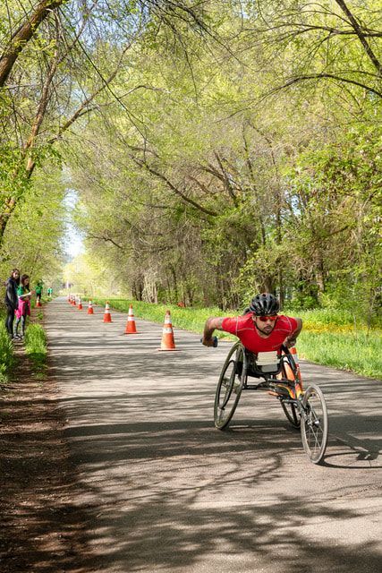 Racer in a red shirt on a long tree-covered course lined with orange cones