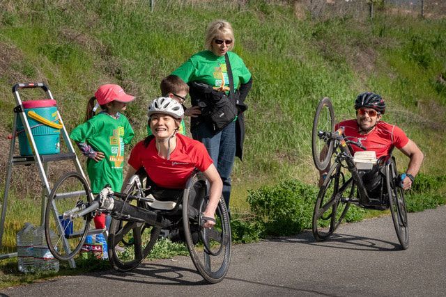 Two racers in red shirts pause by a water station as volunteers in green help