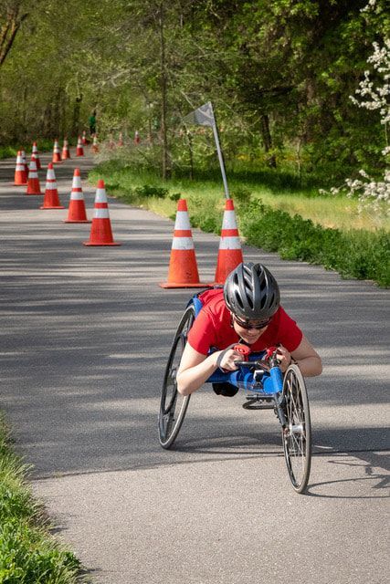 Young racer in a red shirt tucks low in a racing chair along a coned trail