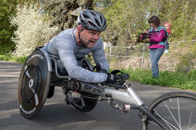 Racer in a gray shirt and silver helmet pushes a racing chair, seen up close