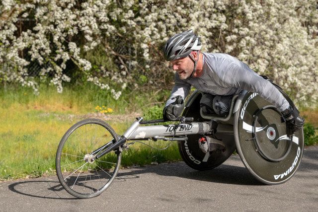 Racer in a gray shirt leans into a turn past bushes of white blossoms