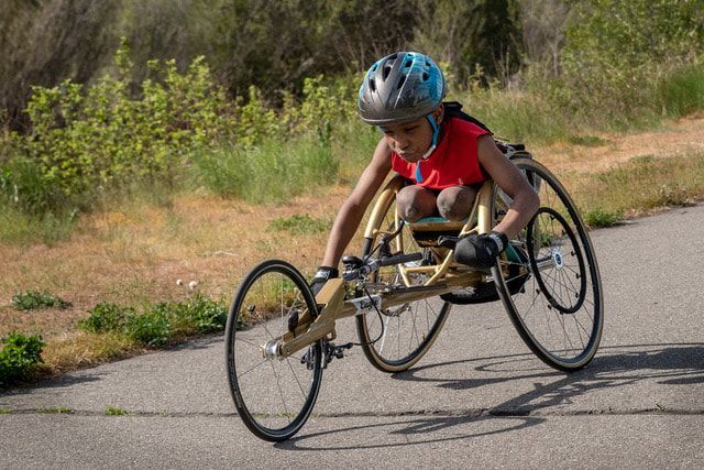 Young racer in a blue helmet grips the wheels of a gold racing chair