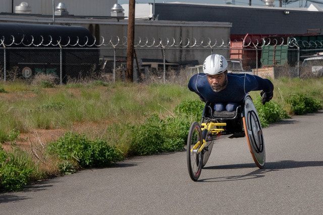 Racer in a navy shirt and white helmet trains by a fenced industrial lot