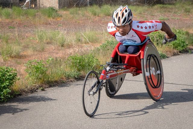 Racer in a stars-and-stripes jersey and red racing chair rounds a bend