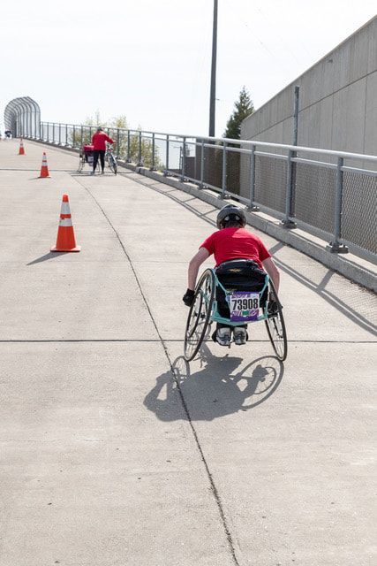 Young racer with a race bib heads along a bridge path, seen from behind