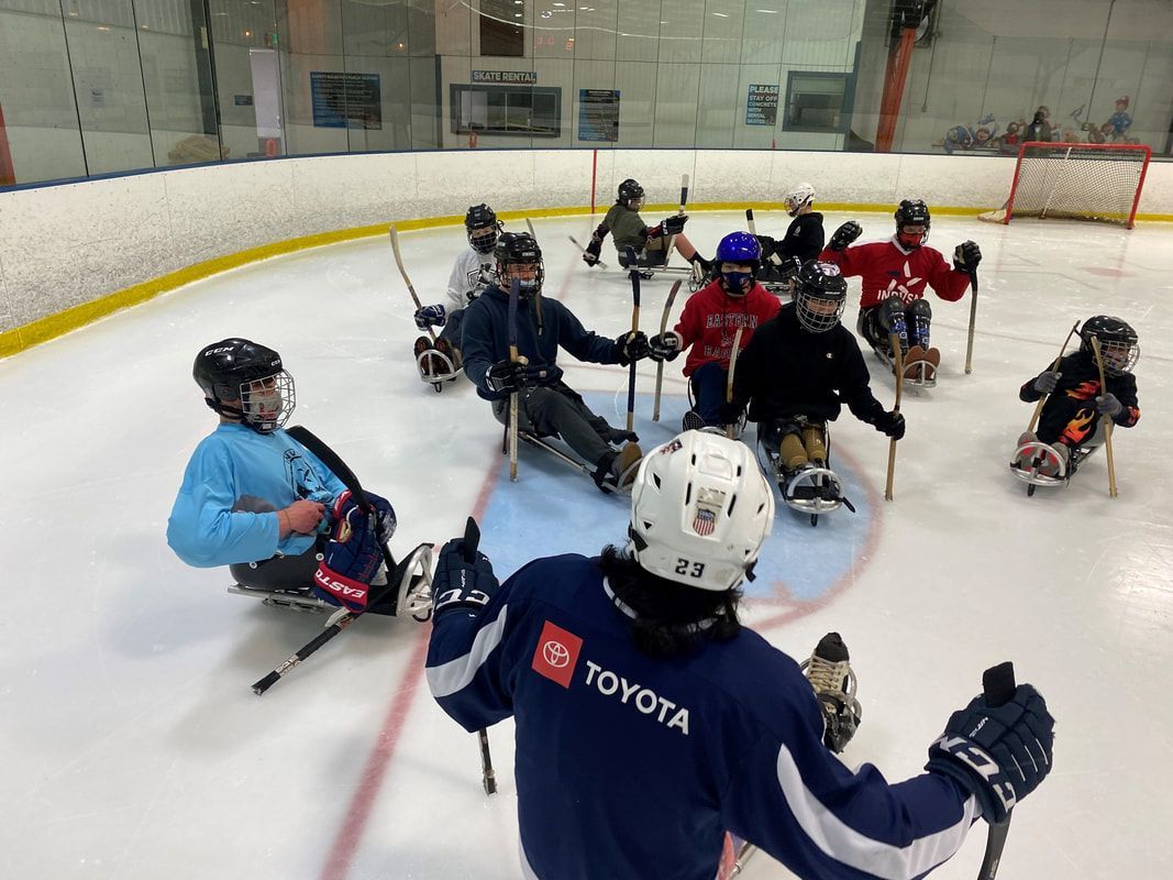 Sled hockey players gather on the ice behind a player in jersey 23