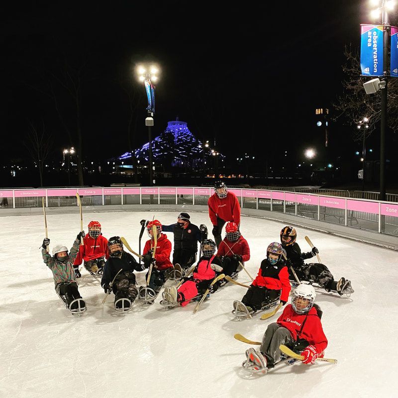 Sled hockey group poses with sticks raised on an outdoor rink at night