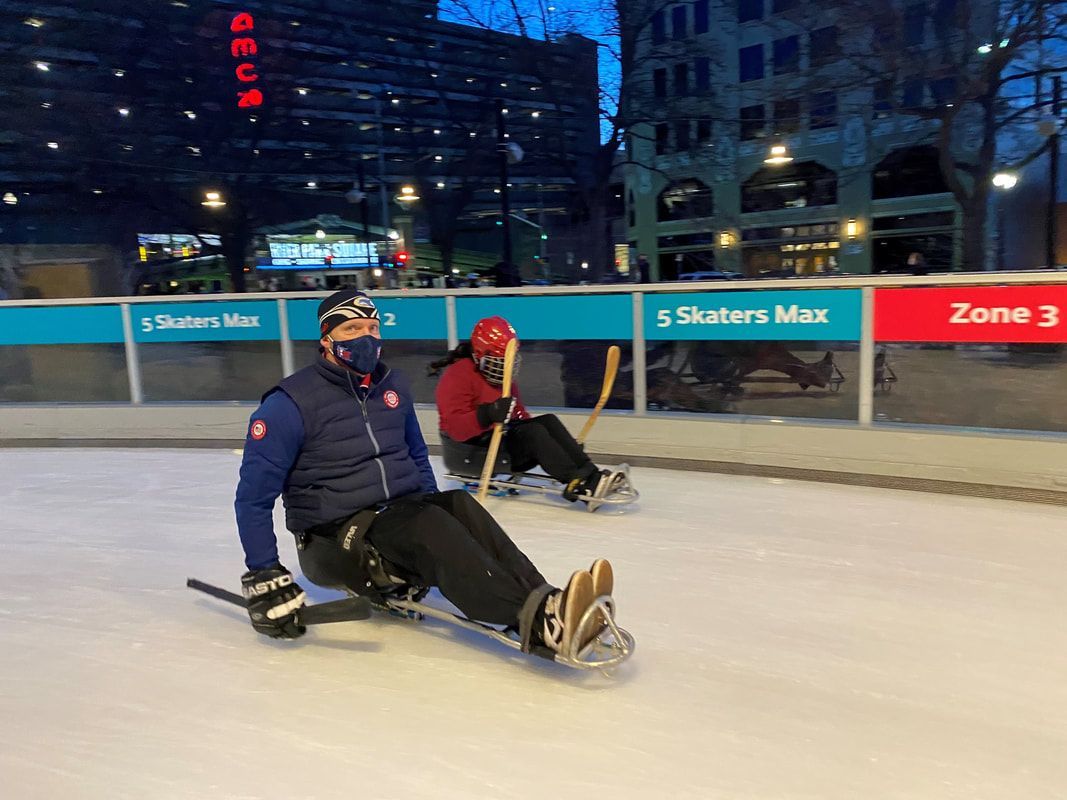 Masked sled hockey player glides on an outdoor downtown rink at night