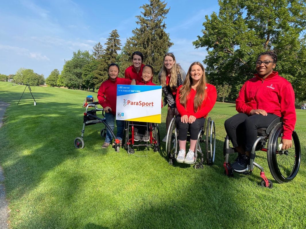 Athletes and staff in red pose on a golf course with a ParaSport event sign