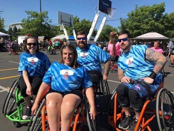 Four adults in blue tie-dye shirts sit in sport wheelchairs at Hoopfest