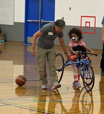 Young girl moves with a blue adaptive bike as a coach walks beside her