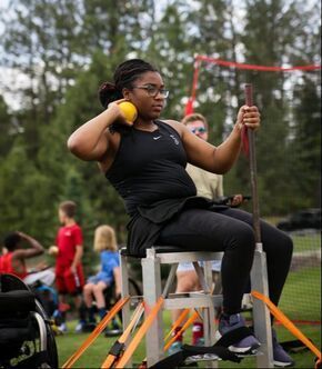 Seated thrower on a throwing frame holds a shot put at the Pine Cone Classic
