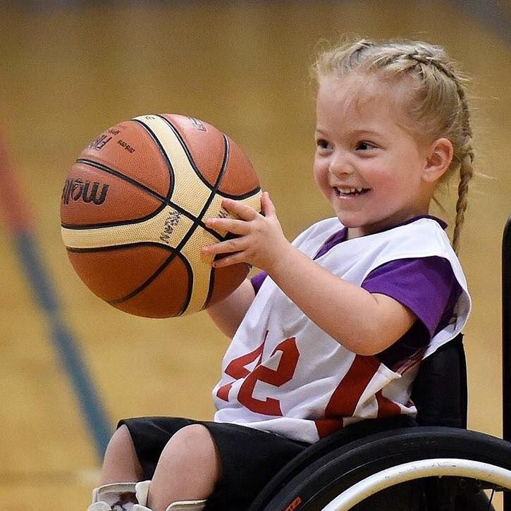 Smiling young girl in jersey 42 holds a basketball in her wheelchair