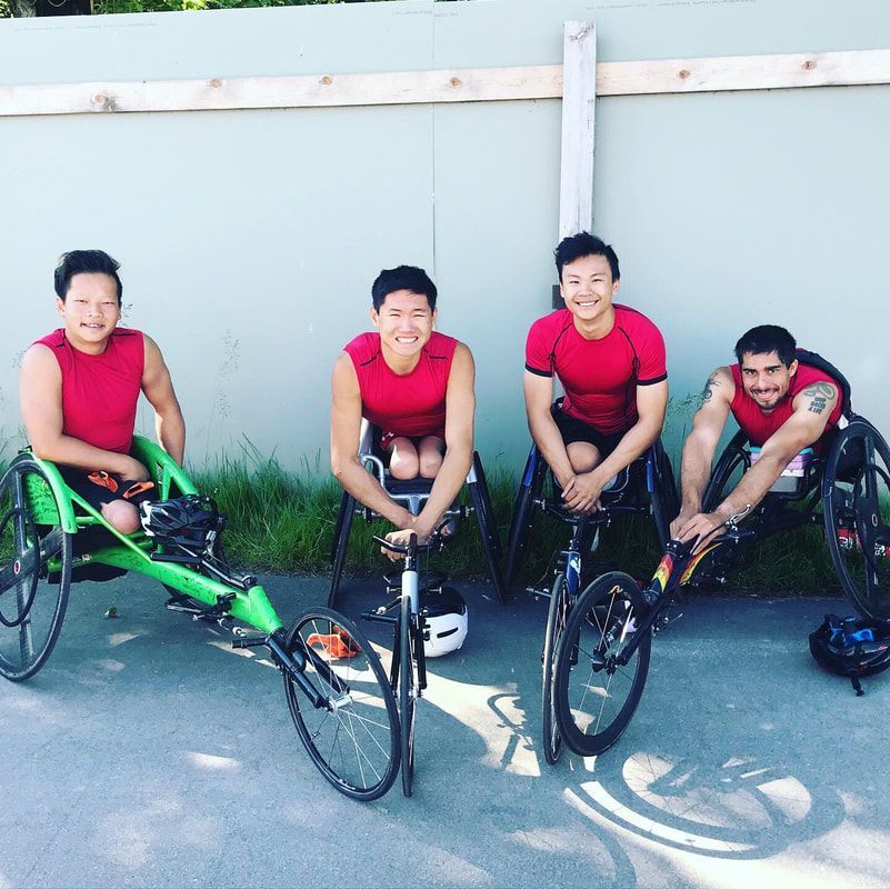Four athletes in red tops sit in racing wheelchairs against a wall