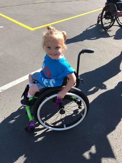 Young child with pigtails smiles from her small wheelchair on the court