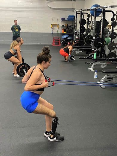 Athlete with a prosthetic leg squats with a resistance band in a weight room