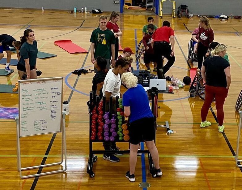 Athletes and coaches gather by the dumbbell rack and workout whiteboard