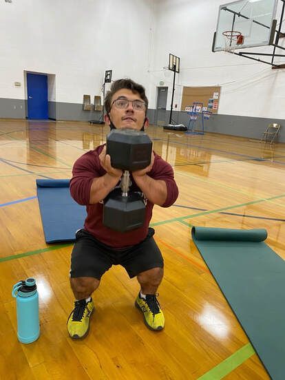 Athlete holds a heavy dumbbell in a deep goblet squat on the gym floor