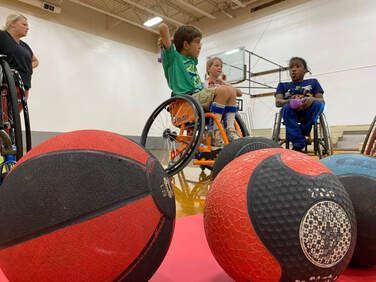 Medicine balls in front of young athletes in wheelchairs in a gym