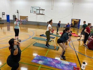 Athletes squat with weights on yoga mats during a group circuit workout