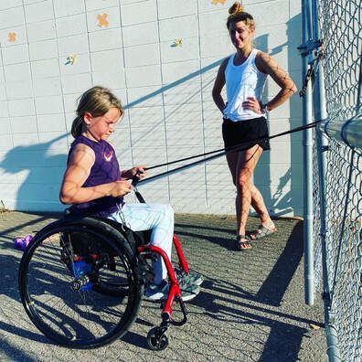 Young athlete in a wheelchair does resistance band rows as a coach watches