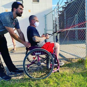 Coach steadies an athlete in a wheelchair doing resistance band pulls outdoors