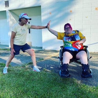 Coach and athlete in a wheelchair press palms together in an outdoor stretch