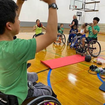 Young athlete in a wheelchair lifts a medicine ball overhead in the gym