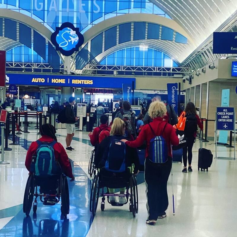Athletes and coaches with backpacks head toward airport security checkpoints