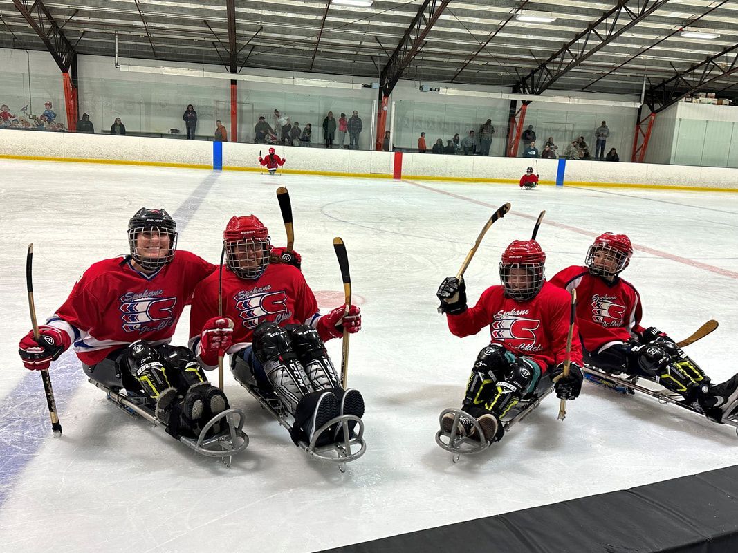 Four sled hockey players in red jerseys raise their sticks and smile