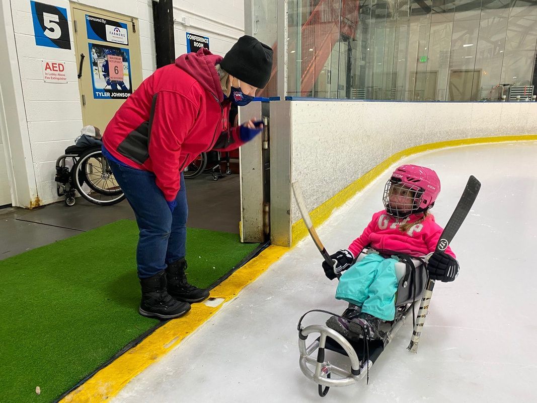Young sled hockey player in a pink helmet chats with an adult at the rink door
