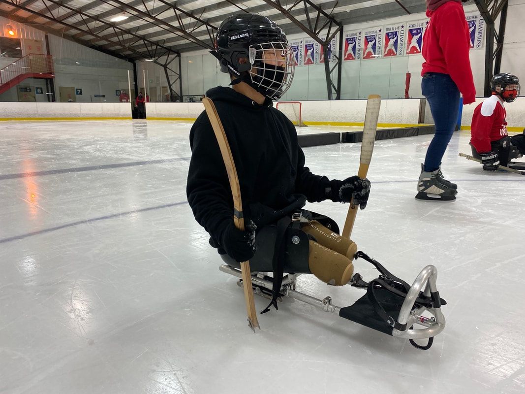 Sled hockey player in a black helmet sits in a sled holding two sticks