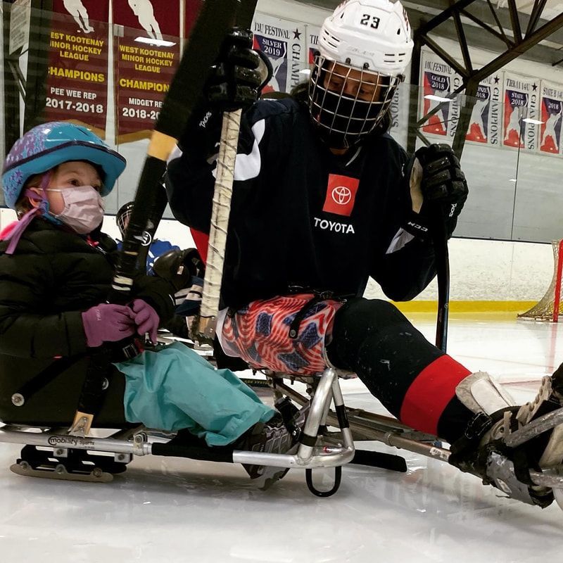 Young sled hockey player in a blue helmet sits beside player #23