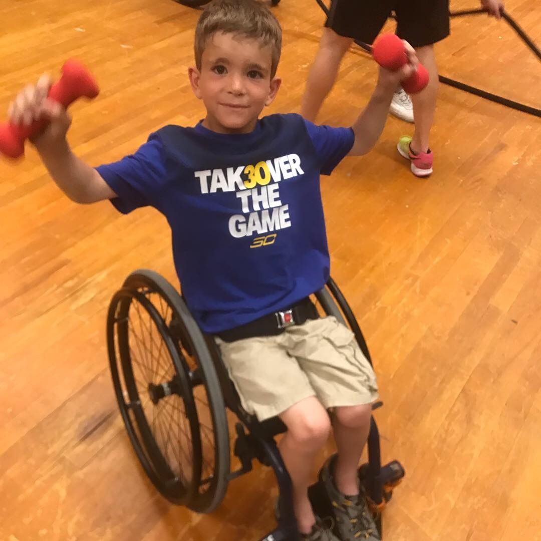 Young athlete in a wheelchair lifts red dumbbells overhead in a gym