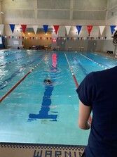 Swimmer trains in a lane of an indoor pool as a coach watches from deck