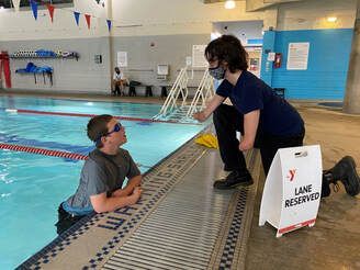 Swimmer at the pool wall talks with a masked coach by a lane reserved sign