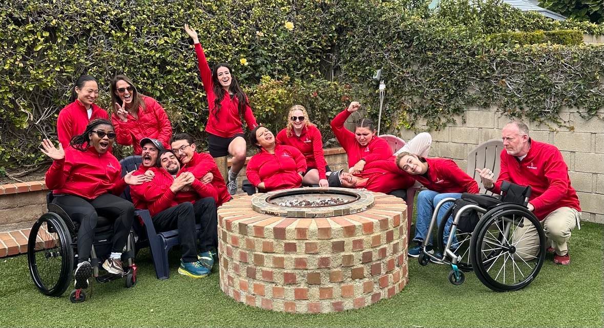 ParaSport Spokane team in red jackets strikes playful poses around a fire pit