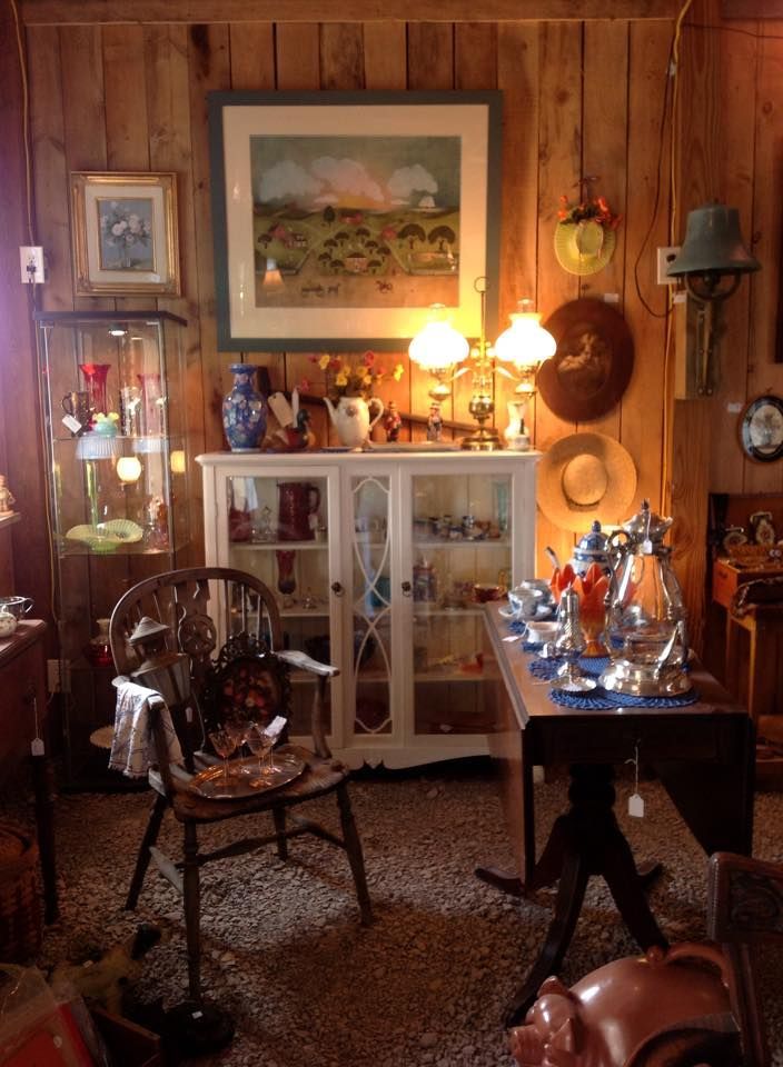 Cozy antique-filled room with wood-paneled walls, lamps, glass cabinets, and a table of decorative items.