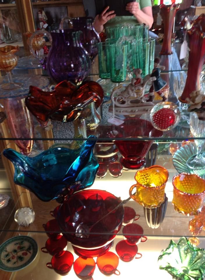 Colorful glass art and dishes displayed on shelves in a shop or market.