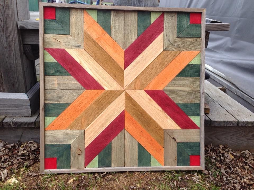 Wooden quilt-style star pattern in red, orange, and green on a square panel outdoors