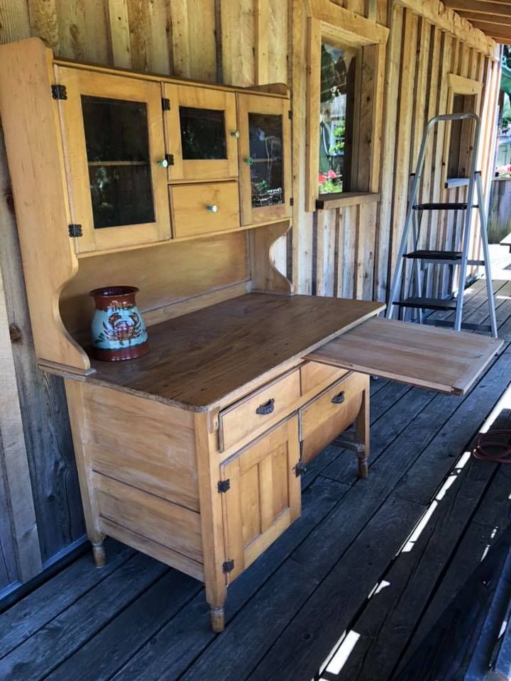Wooden outdoor kitchen cabinet with countertop on a porch, beside a ladder and wooden wall.