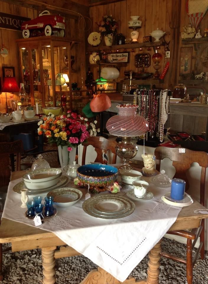 Cluttered antique dining room with a set table, floral centerpiece, and vintage decor on wooden walls