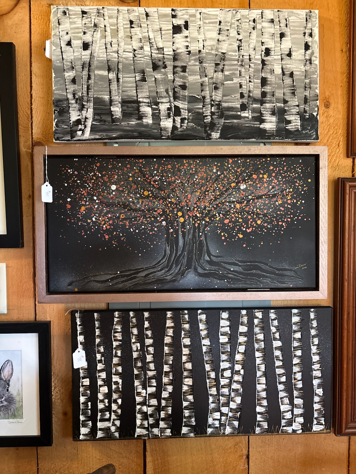 Three abstract tree paintings displayed on a wall, with black, white, and gold tones. Paintings by Dena Martin
