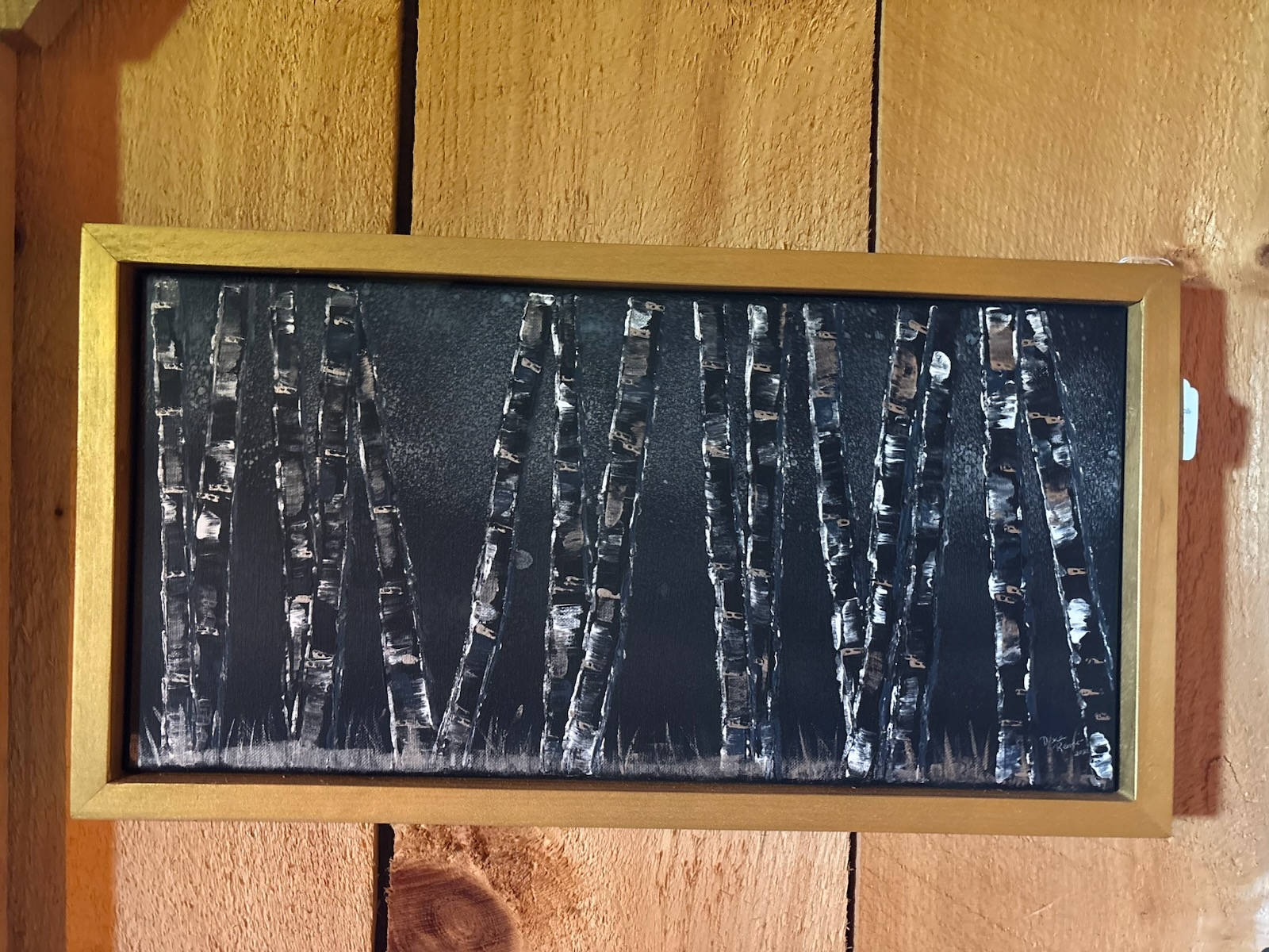 Framed abstract black painting with white birch-like vertical streaks on a wood wall. Paintings by Dena Martin