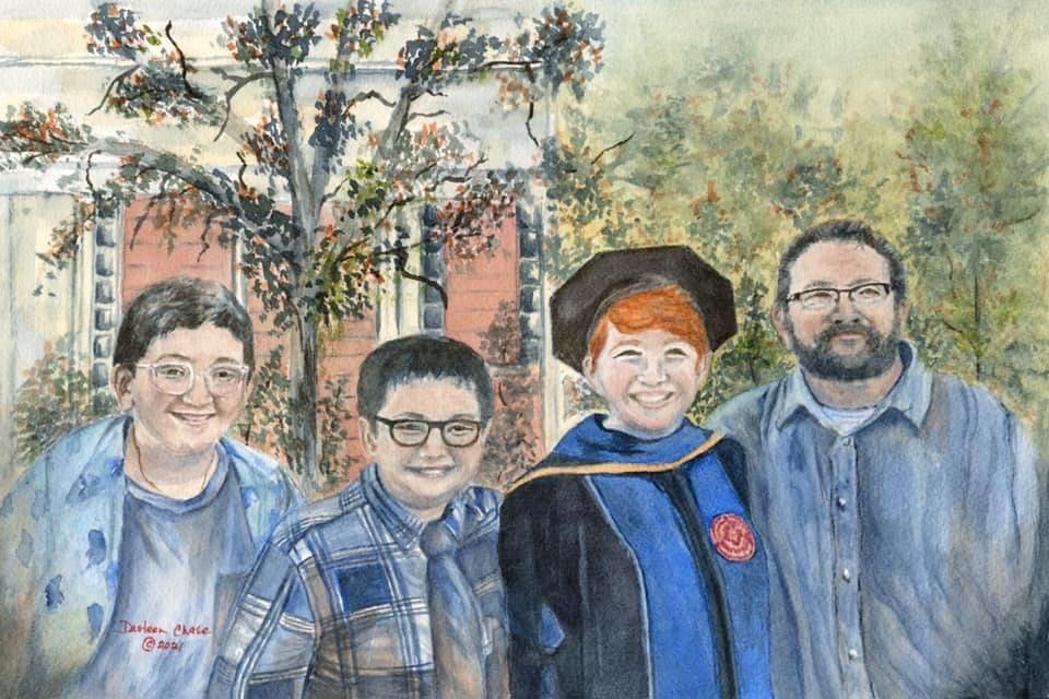 Four people pose smiling outdoors in front of a brick building and trees.