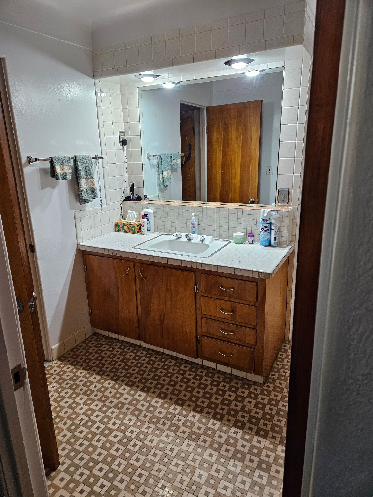 Bathroom with wood vanity, large mirror, white tiled walls, and patterned floor.