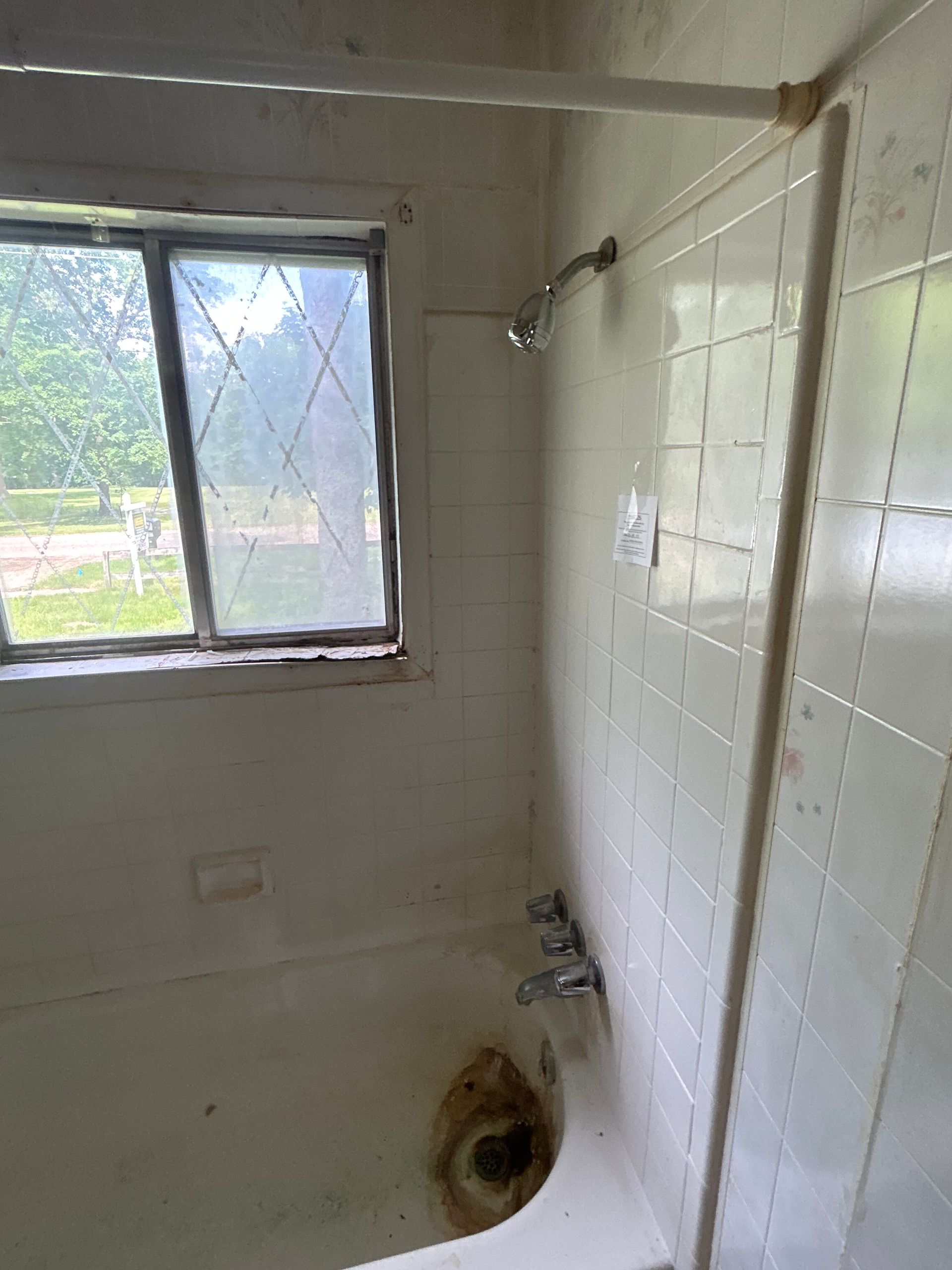 Small tiled bathroom with a window, shower head, and worn sink or toilet fixture.