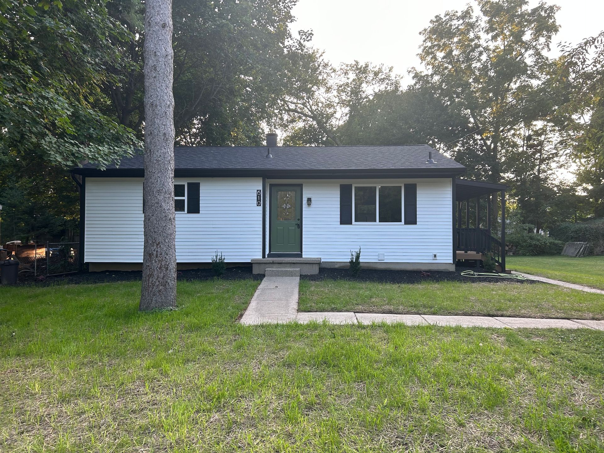 Small white house with green door, front walkway, and large tree in a grassy yard at dusk