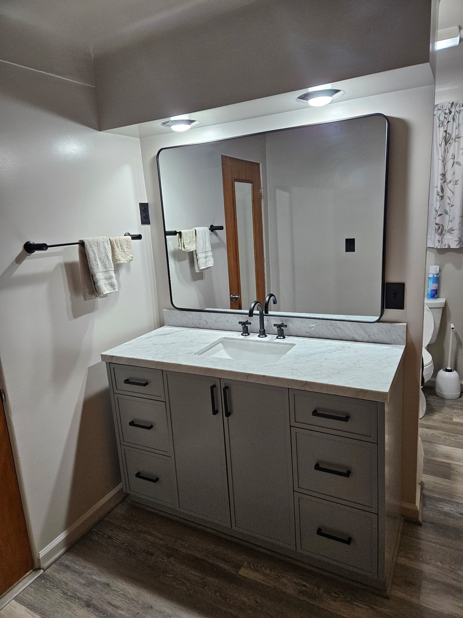 Modern bathroom vanity with large mirror, double sinks, and towel racks under recessed lights