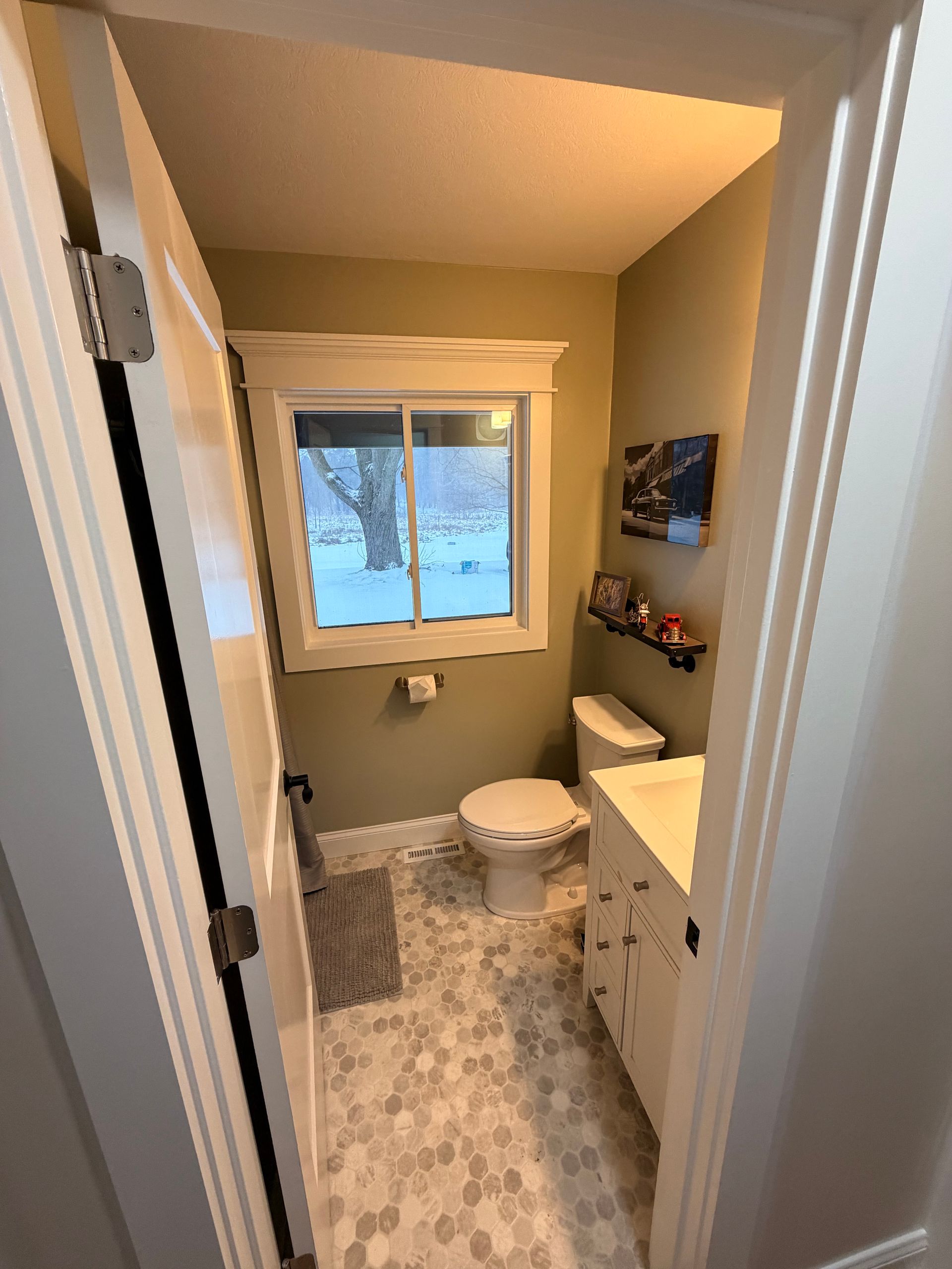 Small beige bathroom with toilet, vanity, window, and patterned floor tile